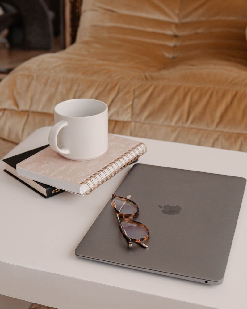 Carnet, tasse, lunettes et ordinateur sur une table basse devant un canapé